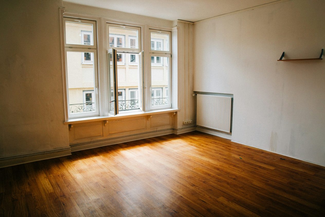 Empty period living room with tall windows and a radiator, before staging